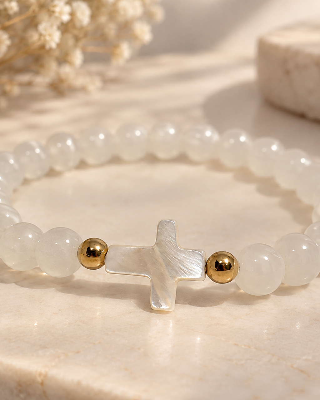 Gros plan sur la croix en nacre du bracelet blanc et doré